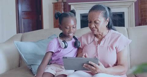Girl with headphones on a tablet, learning a language with an adult alongside her