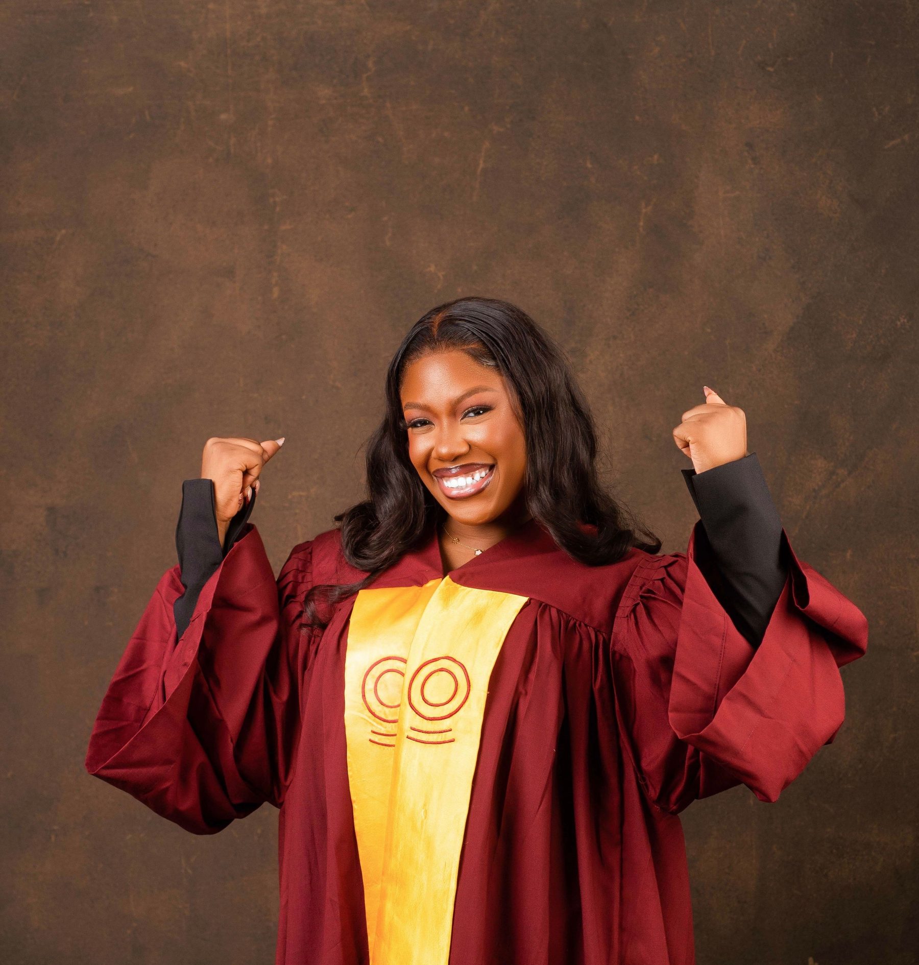 Graduate celebrating in maroon gown with arms raised