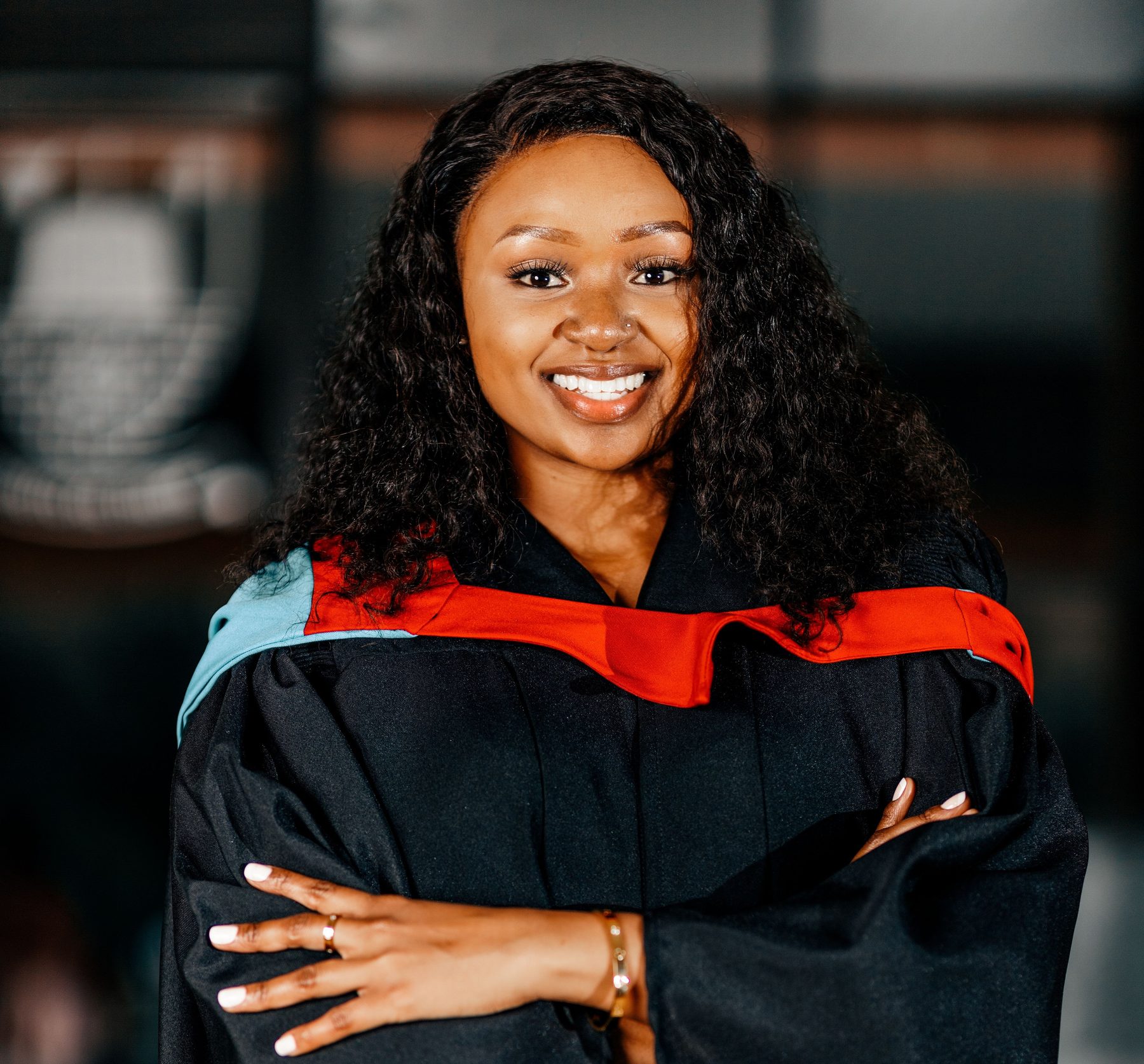 Graduate in gown smiling confidently with arms crossed